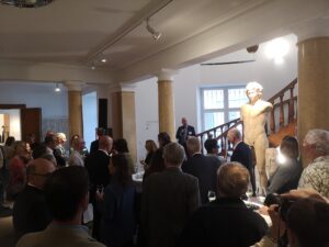Guests listen to Christoph Degen, making a welcome speech on the staircase, next to a male statue.